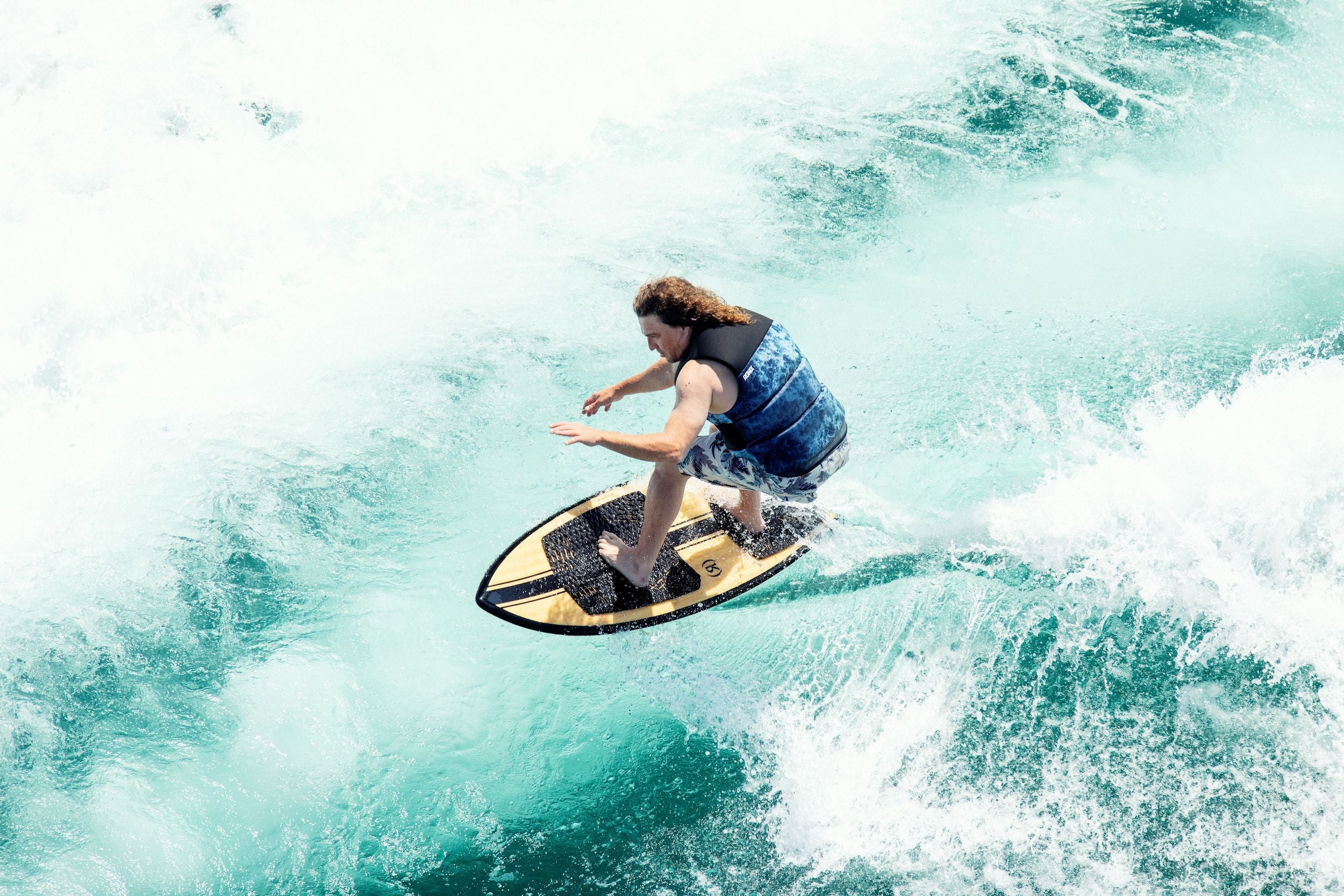 A man on a Ronix 2024 Koal Classic Fish Wakesurf Board riding a wave with great versatility.