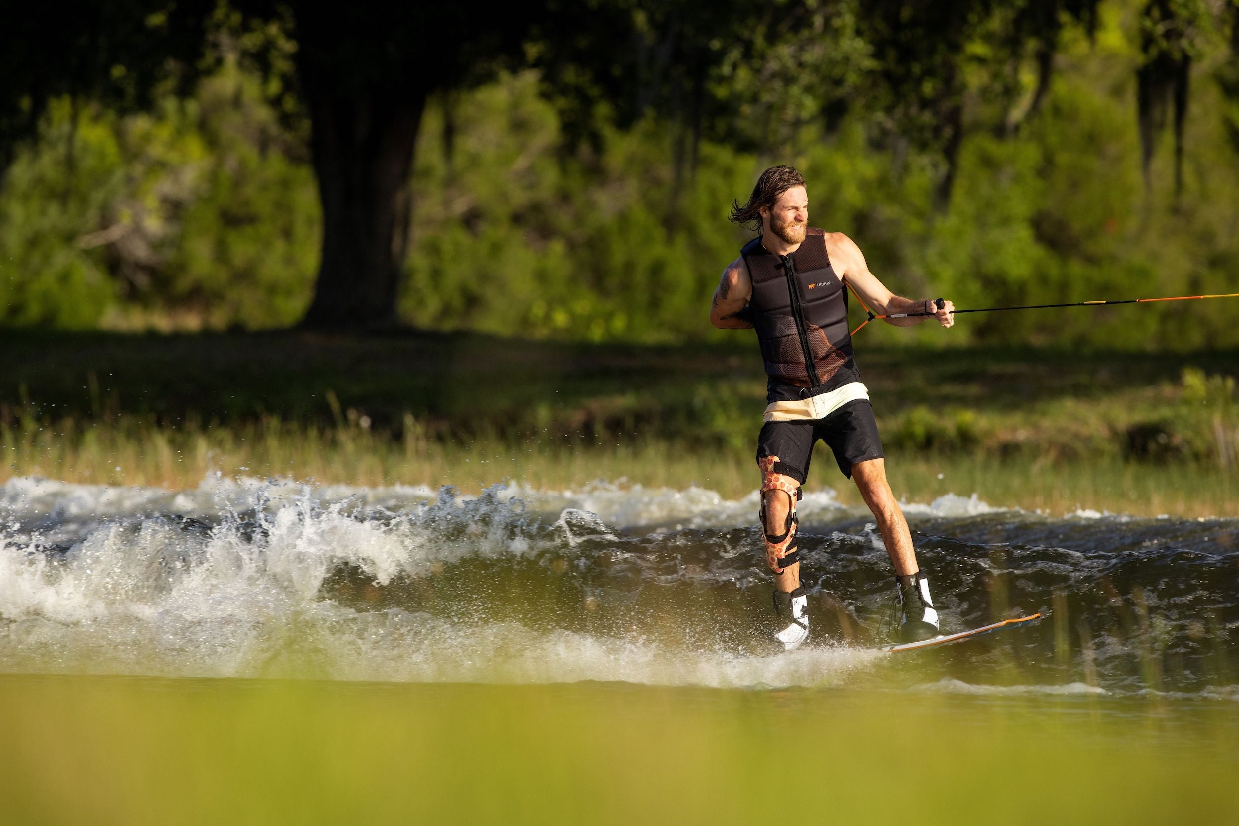 A man is riding a water ski on a lake, wearing Ronix 2023 RXT Boots that offer lightweight flexibility.