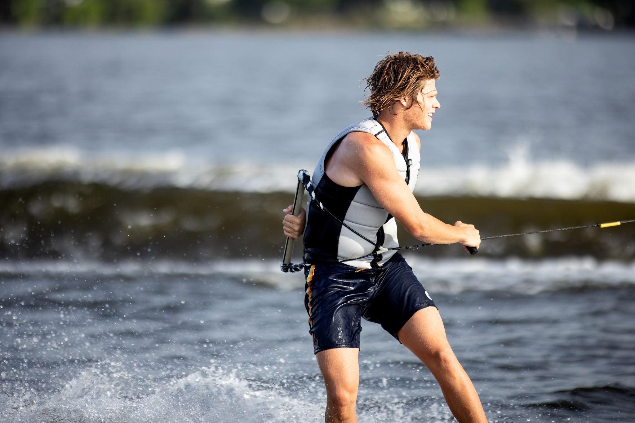A man is sizing his jacket before water skiing on a body of water with the Ronix 2024 Supreme CE Approved Impact Vest.