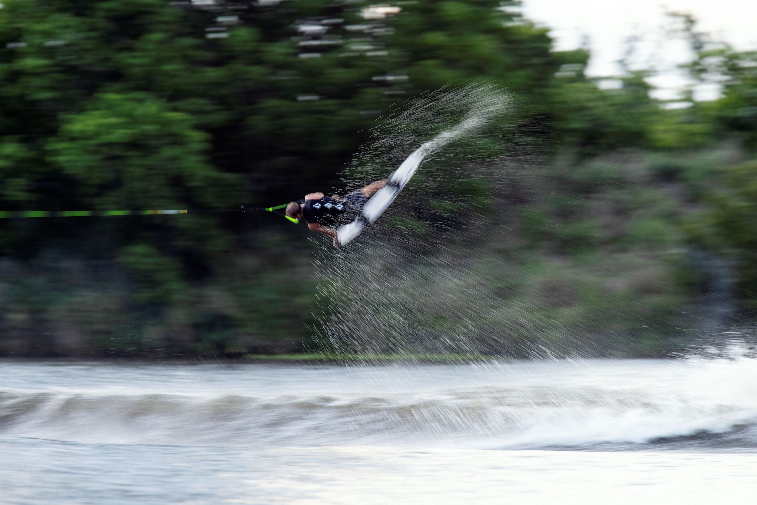 A person is riding a wakeboard in the water while wearing a Ronix 2024 Volcom Men's CE Impact Vest made of 4-way stretch material.