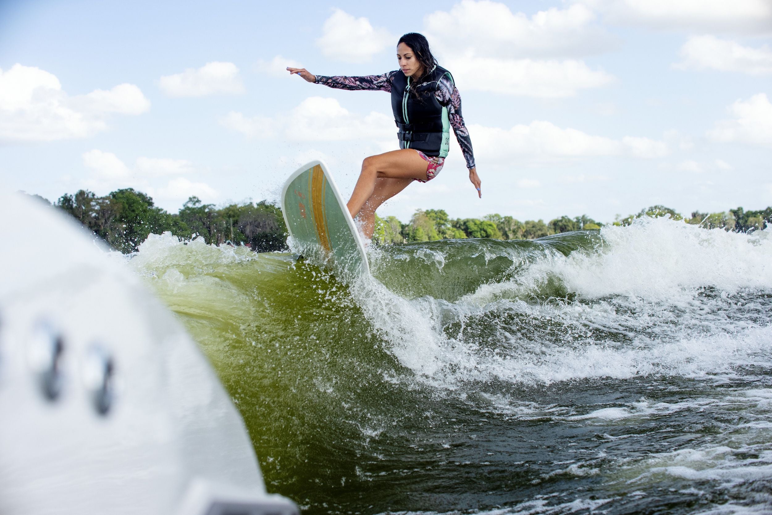 A woman effortlessly riding a wave on a Ronix 2024 Women's Koal Fish Wakesurf Board with surf style.