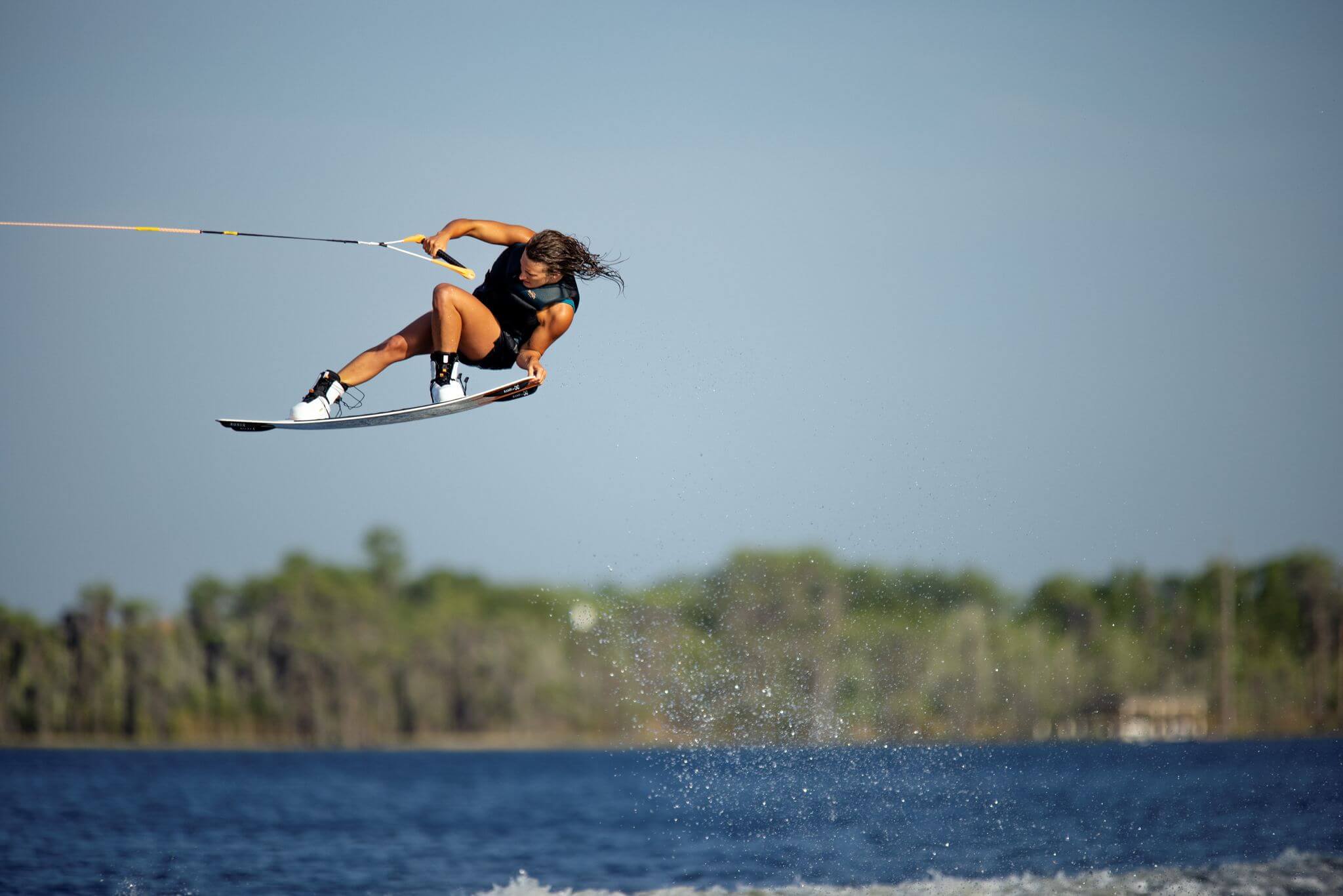 A woman is riding a wakeboard in the air, showcasing the amazing performance of the Ronix 2023 Women's Rise Bindings equipped with an Intuition+ liner.