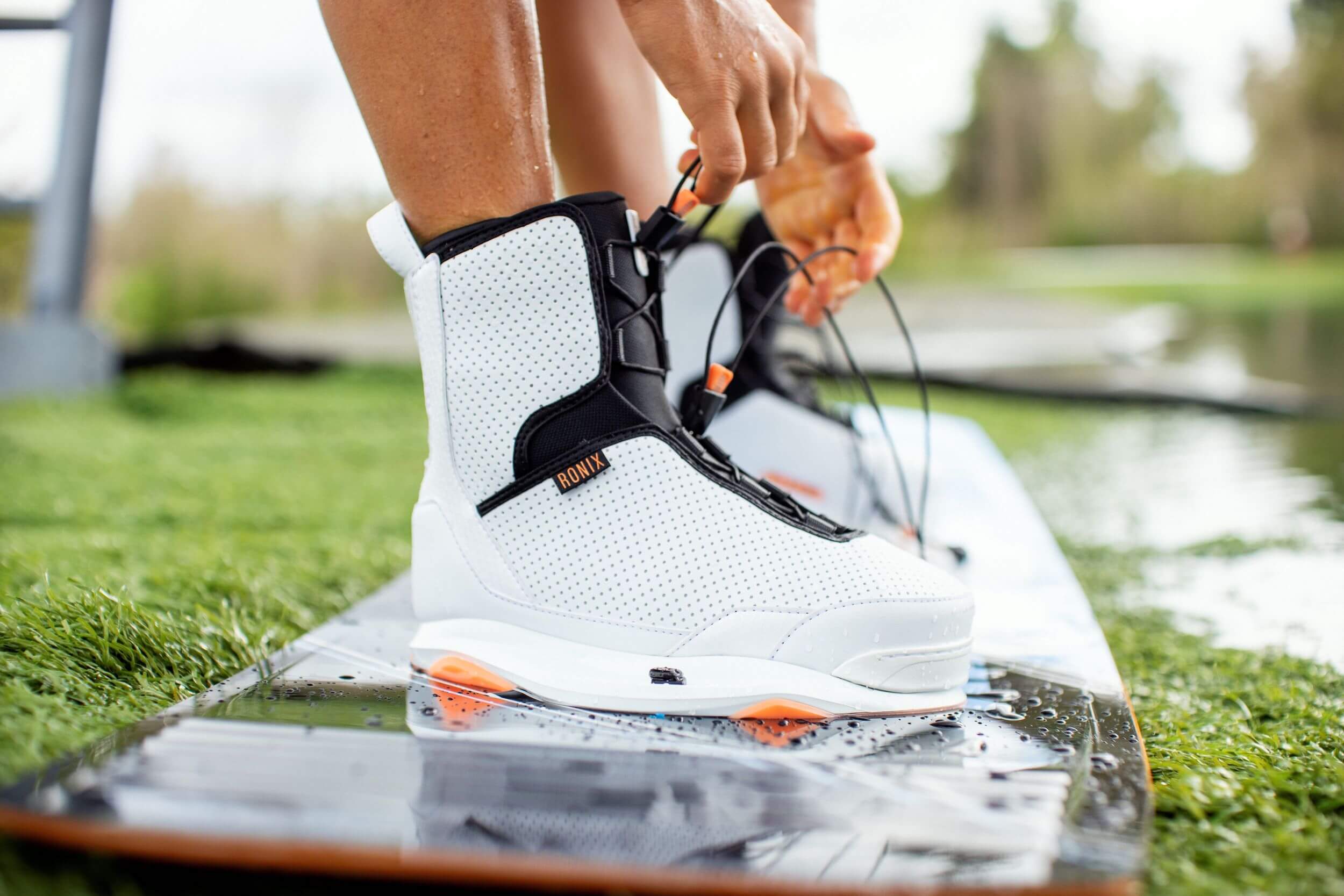 A person is putting on a pair of Ronix 2023 Women's Rise Bindings featuring Intuition+ liner.