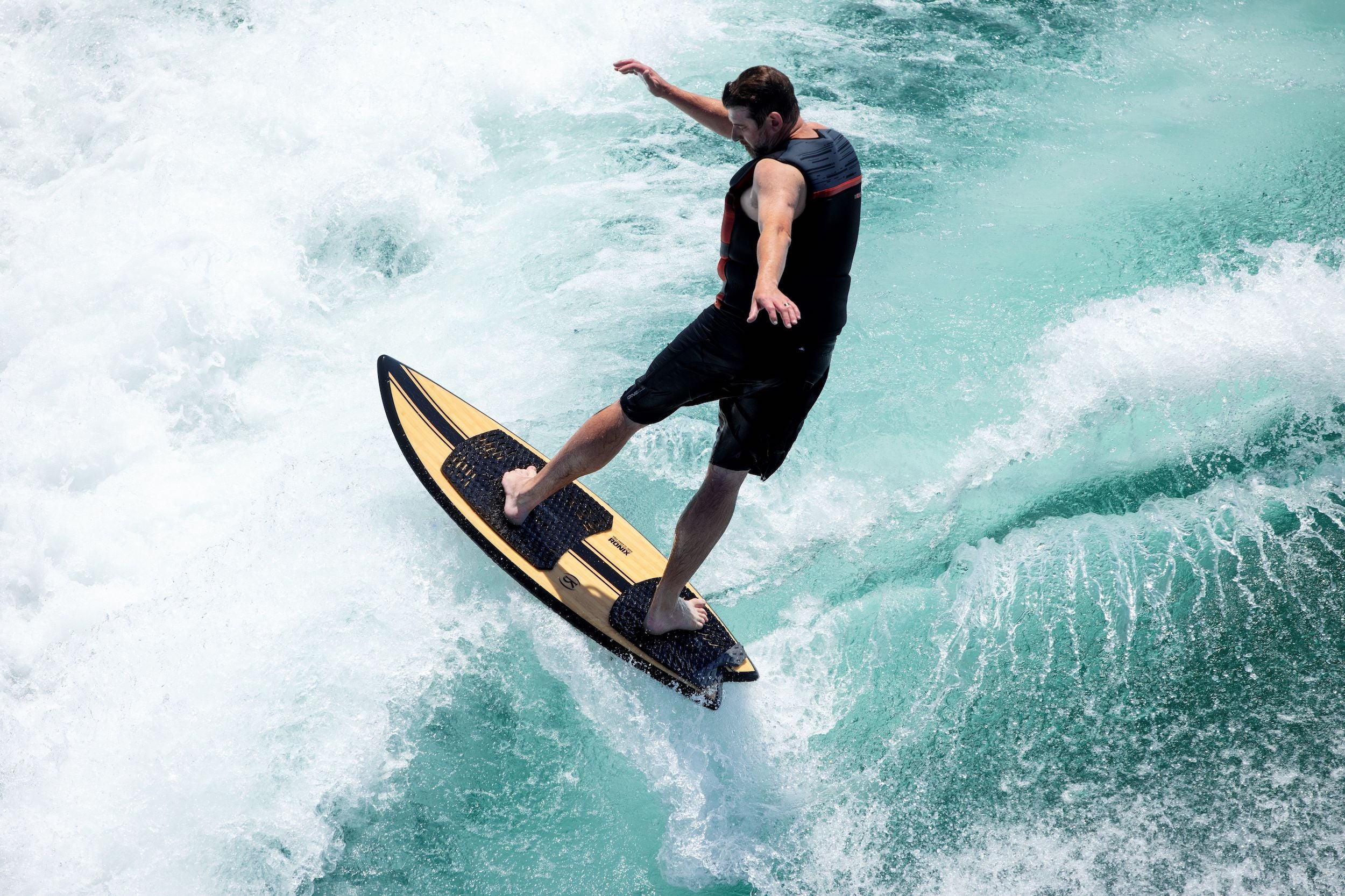 A man riding a wave on a surfboard while wearing a Ronix Megacorp Capella 3.0 Men's CGA Vest.