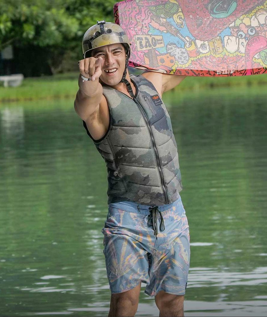 A man in a Liquid Force Squad Tao Heritage Comp Vest - Camo holding a wakeboard in the water.
